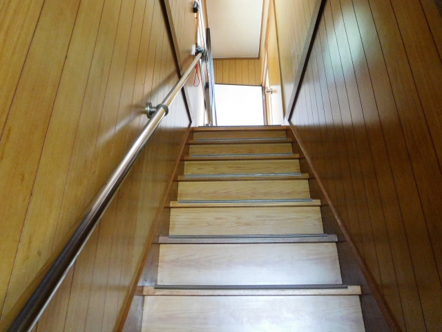 Wooden stairwell with a metal handrail on the left, wood-paneled walls, stairs leading up to a bright doorway.